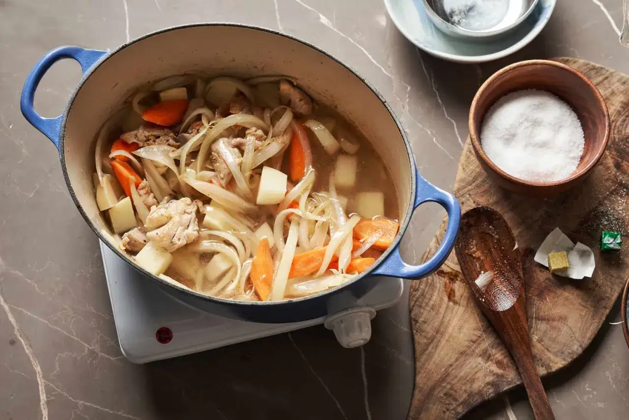 A hearty Japanese white stew simmers in a blue pot, filled with chicken, potatoes, carrots, and onions.