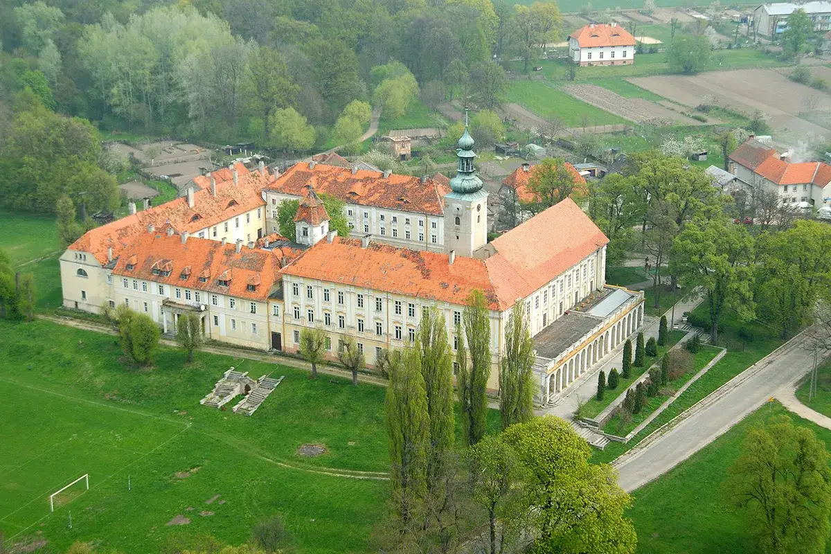 Rozległy zespół pałacowy w Oleśnicy Małej z charakterystyczną wieżą i pomarańczowymi dachami, otoczony zielenią i polami.