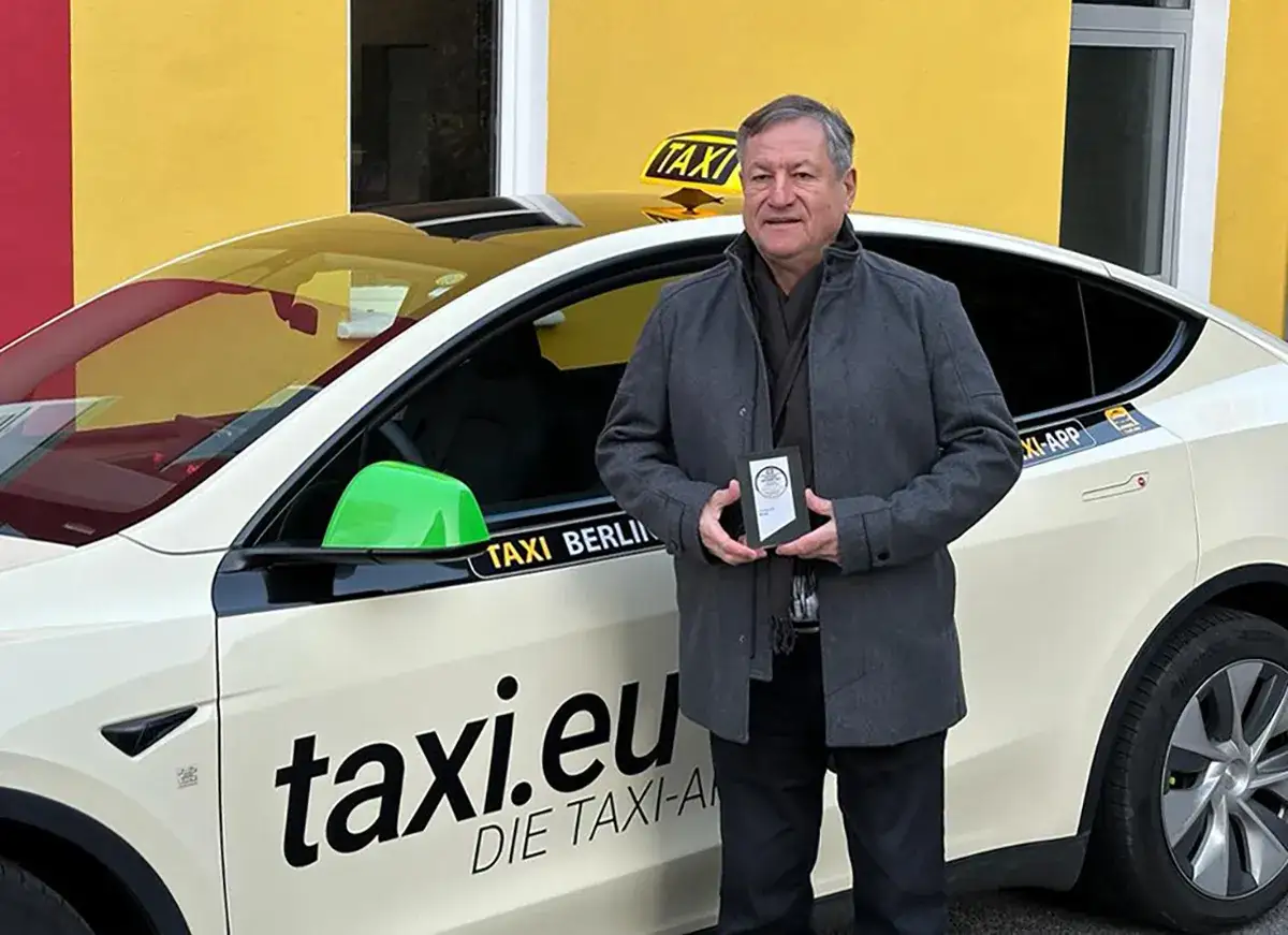 Mann vor einem wei&szlig;en Taxi mit der Aufschrift 