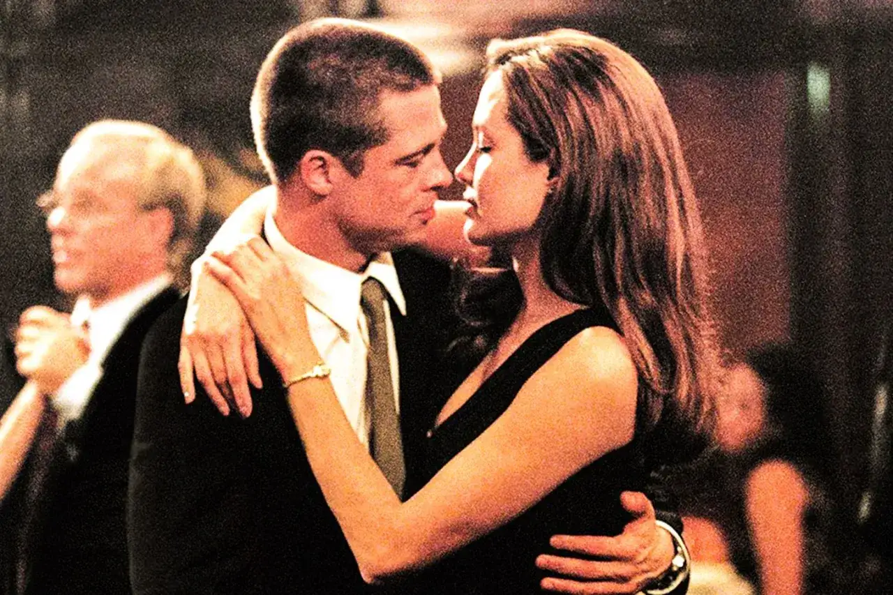 Angelina Jolie i jej mąż Brad Pitt w romantycznym uścisku, w tle inni goście na przyjęciu.