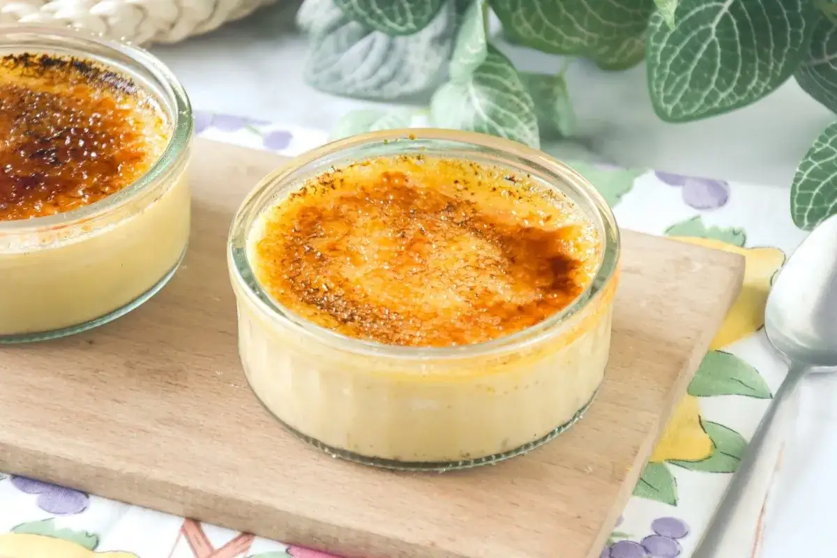 Dos cremosos postres de creme brulee en vasitos de cristal, con una capa superior de azúcar caramelizado dorado y crujiente.