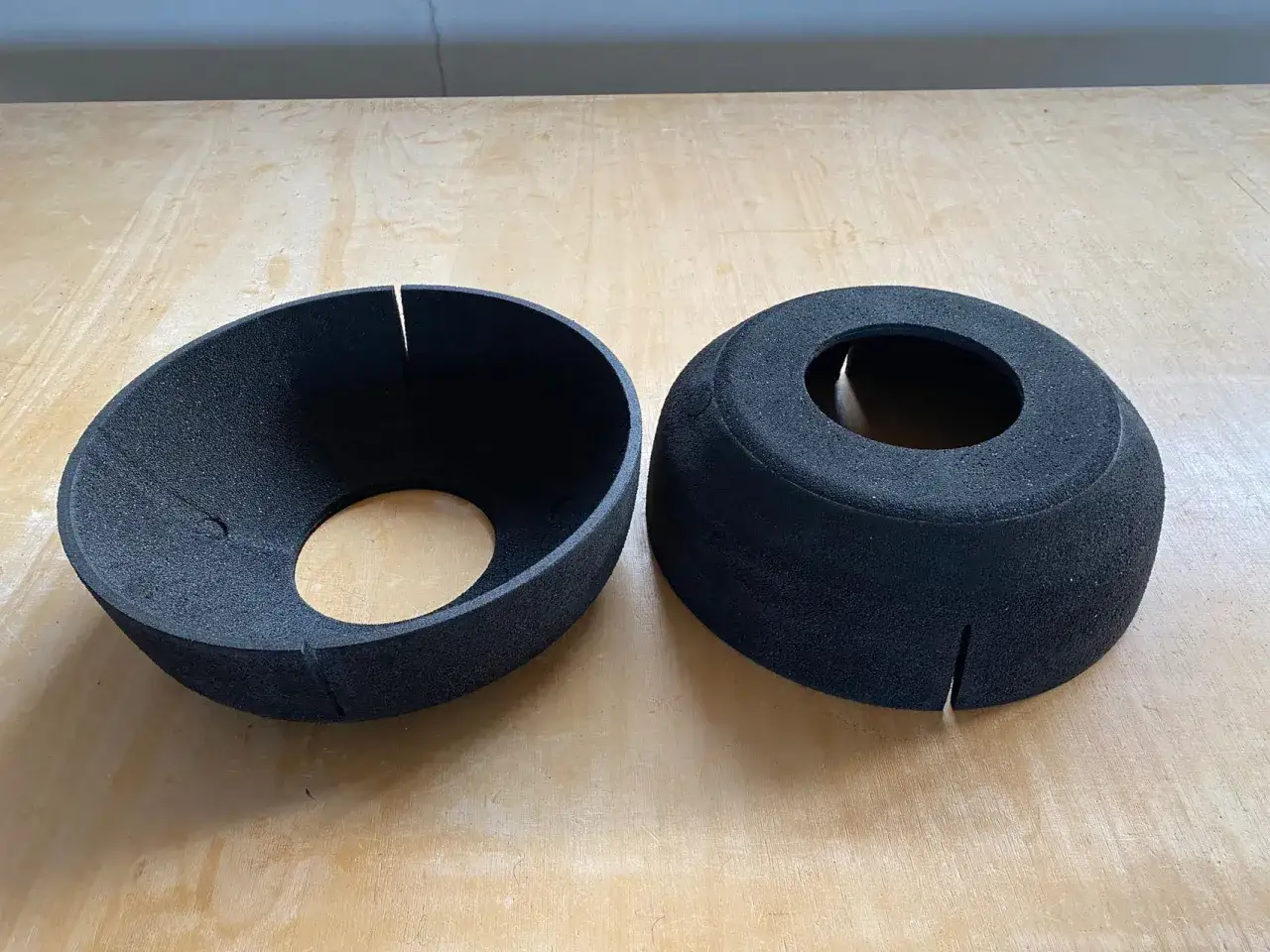 Zwei schwarze EPP-Platten, geformt wie Trichter oder Kappen, liegen auf einer Holzoberfläche.