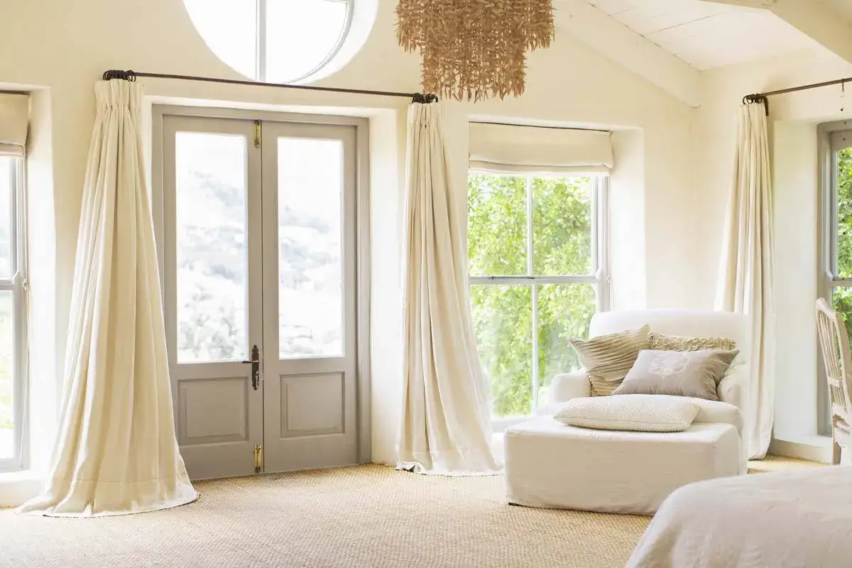 Tende color crema scendono dal soffitto, incorniciando porte e finestre. L'altezza del bastone tende dal soffitto è ottimale per un look arioso.