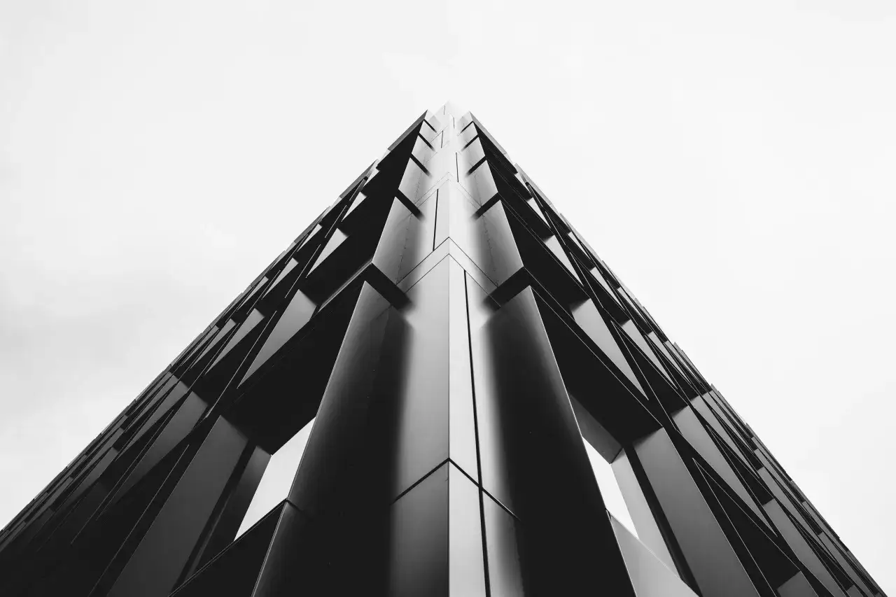 Nowoczesny budynek z geometrycznymi elementami, widziany z dołu, tworzy wrażenie nieskończoności. Perspektywa żabia podkreśla jego monumentalność.