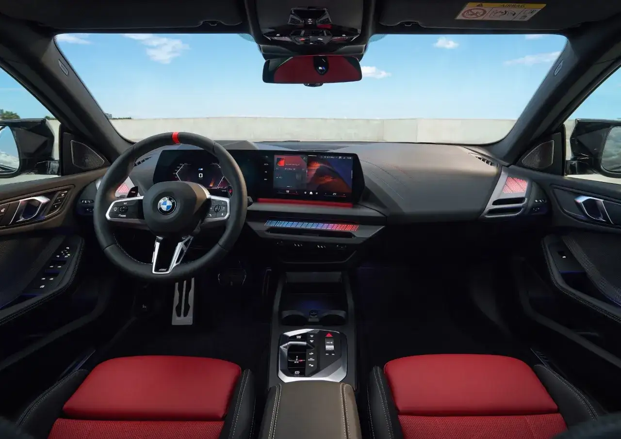 Wnętrze BMW 218i z czerwonymi akcentami na siedzeniach i kierownicy. Nowoczesny kokpit z dużym ekranem multimedialnym i kolorowym podświetleniem.