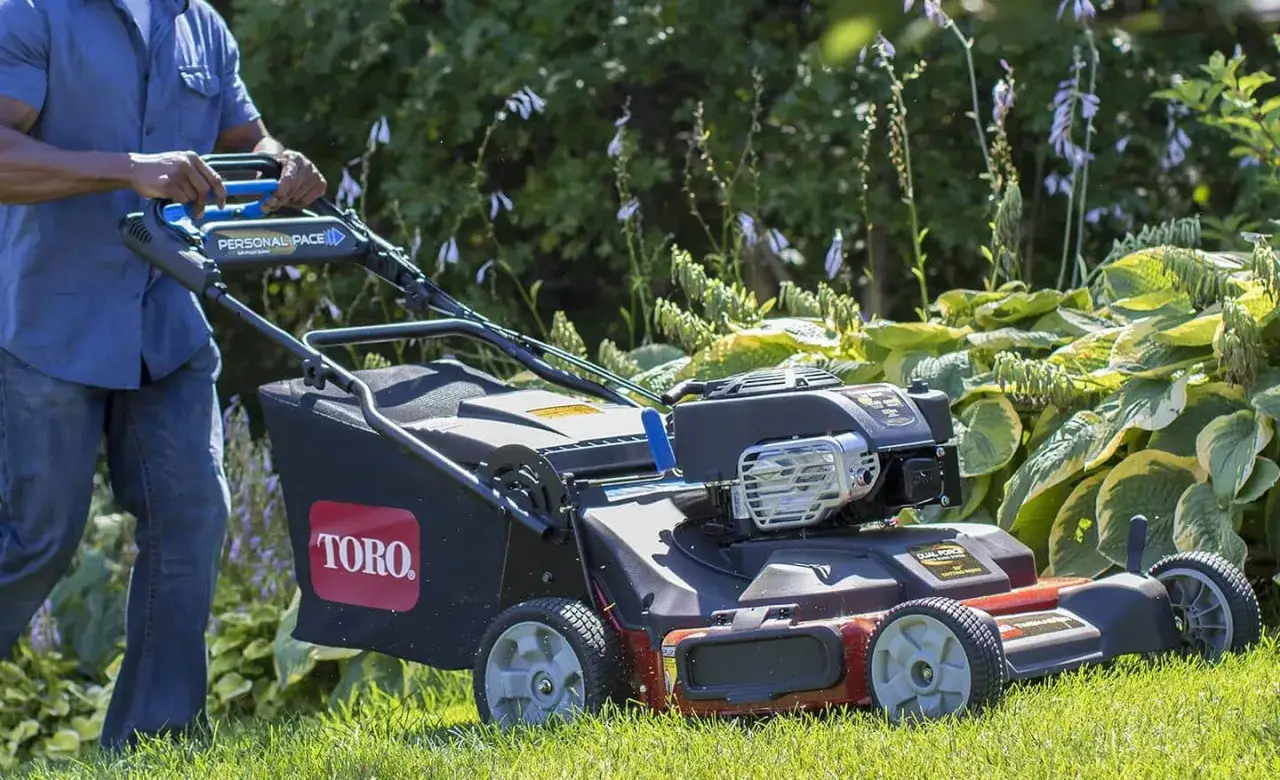 Mężczyzna pcha kosiarkę spalinową Toro po trawniku. Wybór między kosiarką elektryczną czy spalinową zależy od potrzeb.