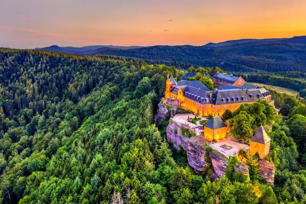 Château illuminé perché sur une falaise, entouré par la plus belle forêt de France au coucher du soleil.