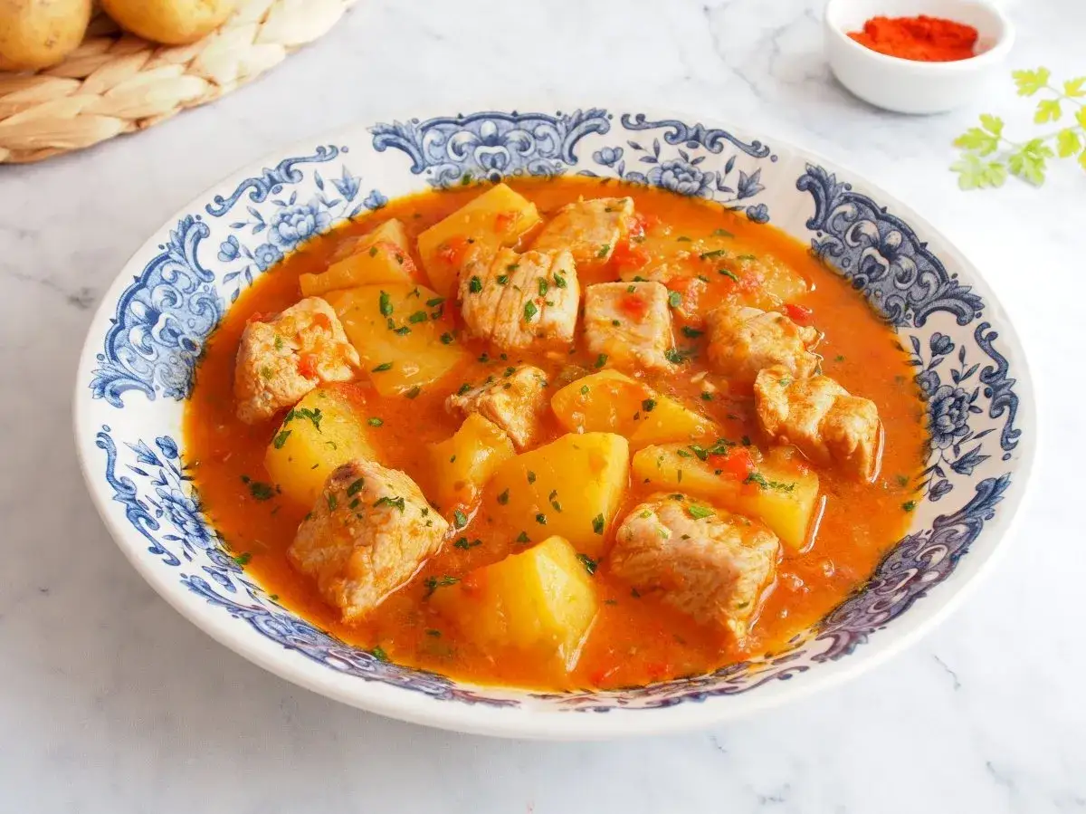 Un delicioso marmitako de at&uacute;n con patatas y pimientos rojos en una fuente decorada.