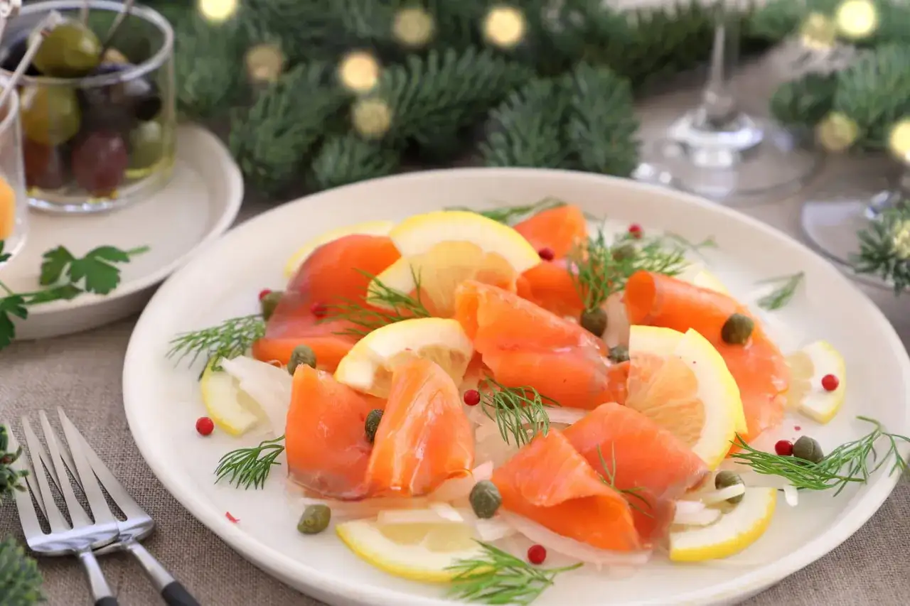 Belle présentation de saumon fumé sur une assiette, décorée de citrons, câpres et aneth. Parfait pour un Noël festif.