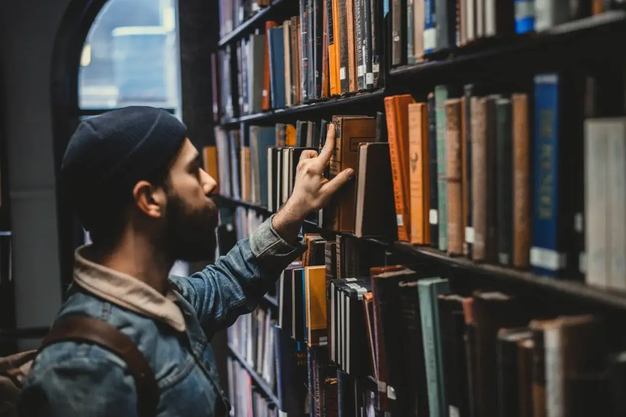 Studente con barba sceglie un libro da una libreria, forse per la sua laurea in legge o giurisprudenza.