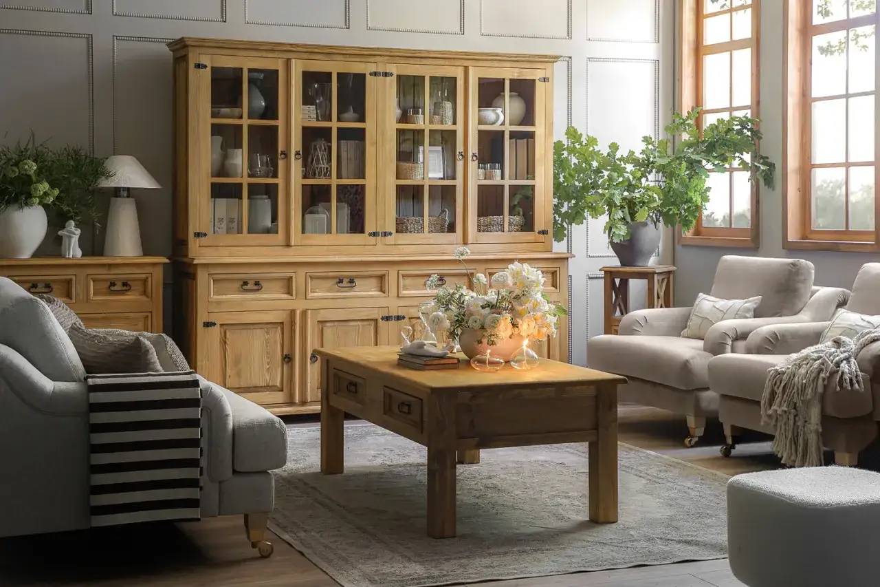 Przytulny salon w stylu farmhouse z drewnianą komodą, wygodnymi fotelami i bukietem kwiatów na stoliku.