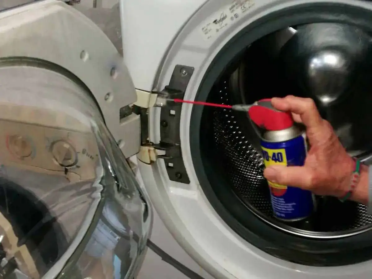Mano spruzza WD-40 sulle cerniere della lavatrice per lubrificare e facilitare la pulizia dell'obl&ograve;.