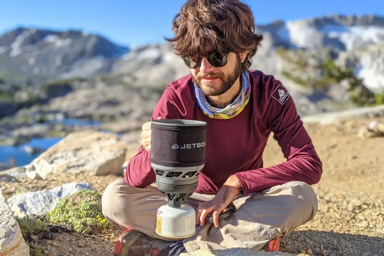 Man med Jetboil-k&ouml;k njuter av mat p&aring; vandring i bergig terr&auml;ng.