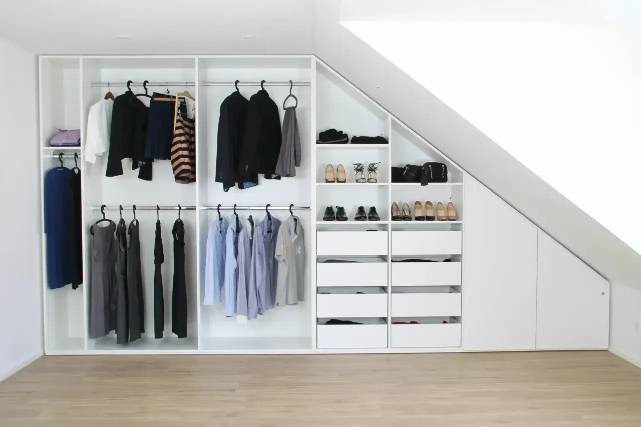 Ein maßgefertigter Kleiderschrank bauen, der sich perfekt in die Dachschräge einfügt. Ordentlich sortierte Kleidung und Schuhe.