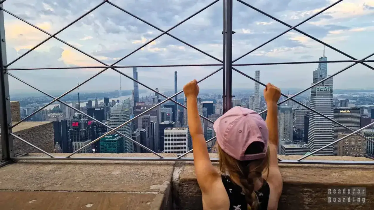 Dziecko z podniesionymi rękami podziwia panoramę Nowego Jorku. Zastanawia się, ile pięter ma Empire State Building, patrząc na inne wieżowce.