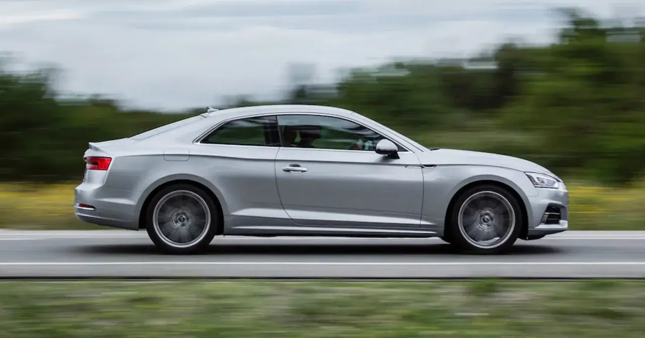 Srebrne Audi A5 Coupe w ruchu, z rozmytym tłem zieleni i nieba.