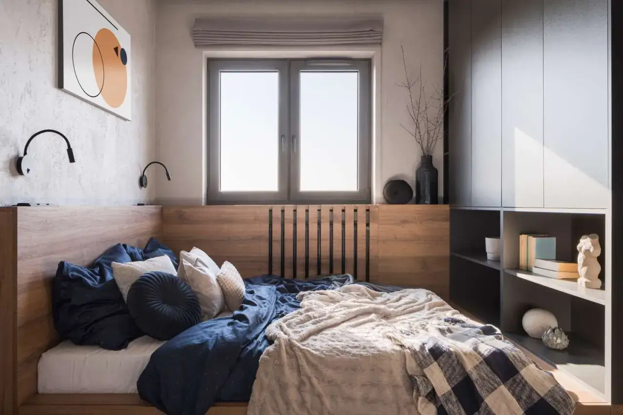 A cozy bedroom with a wooden headboard, navy bedding, and a fluffy throw. This design shows how to make a small bedroom look bigger with light colors and smart storage.