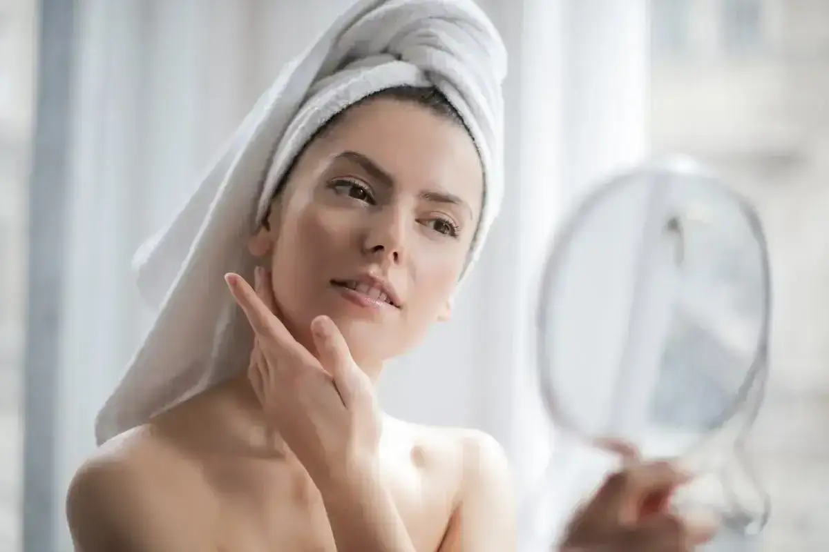 Frau mit Handtuch auf dem Kopf streicht sich über das Gesicht, das eine makellose glass skin zeigt. Sie blickt in einen Spiegel.