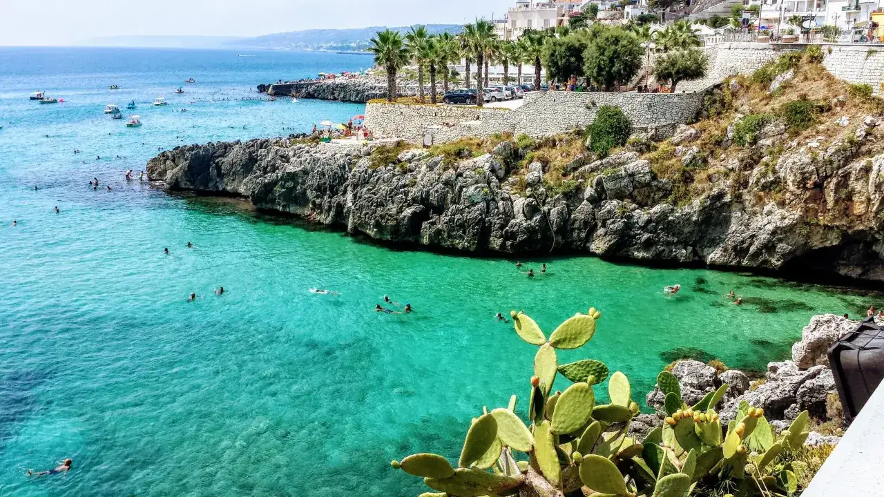 Plage rocheuse avec des eaux turquoise cristallines, des palmiers et des figues de barbarie. Des baigneurs profitent du soleil et de la mer &agrave; Castro, Italie.