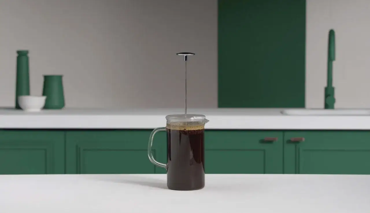 En presskanna med m&ouml;rkt kaffe st&aring;r p&aring; en vit b&auml;nk. En gr&ouml;n k&ouml;ksinredning syns i bakgrunden. Perfekt f&ouml;r att brygga presskaffe.