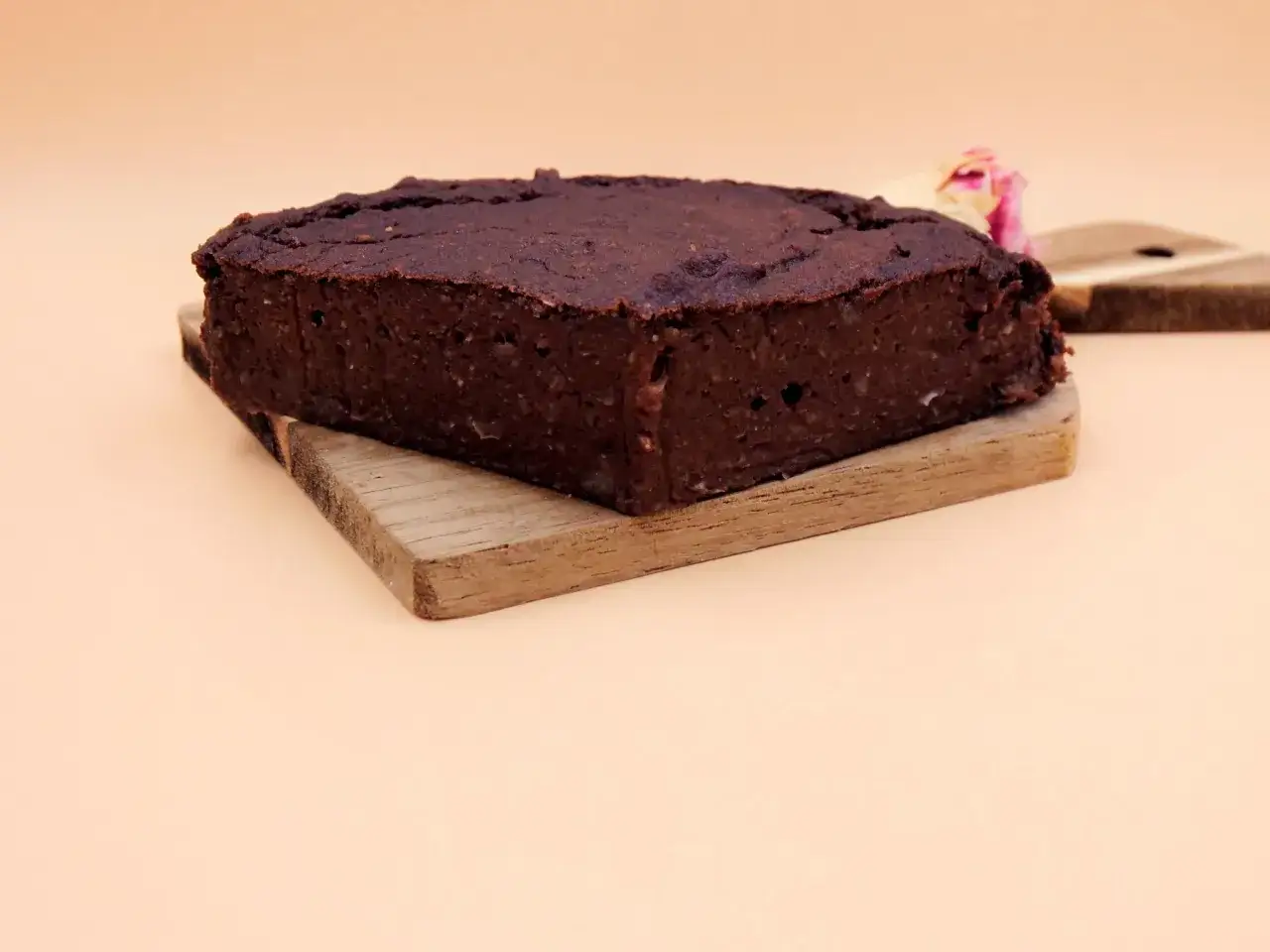 Czekoladowy brownie z ciecierzycy, wilgotne i puszyste, na drewnianej desce. Obok delikatny pączek róży.