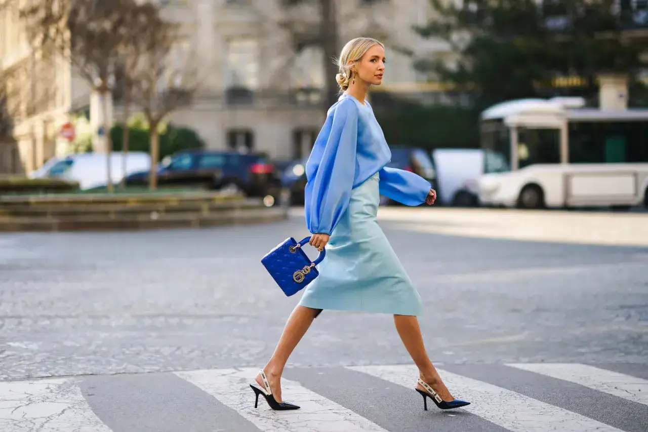 Donna con abito e borsa blu, un look elegante in carta da zucchero colore, attraversa la strada.