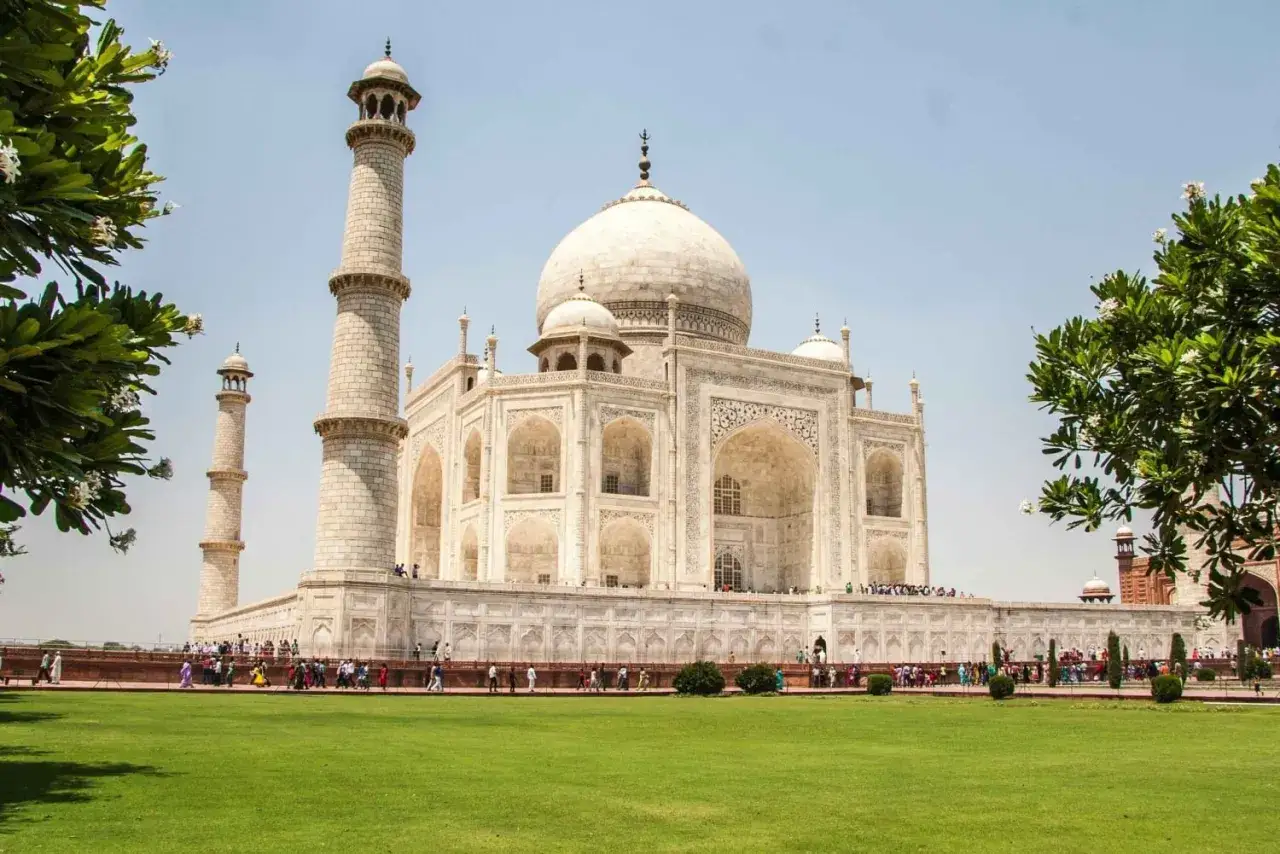 Majestatyczny Taj Mahal w Indiach, biały marmur lśni w słońcu, otoczony zielonym trawnikiem i drzewami.