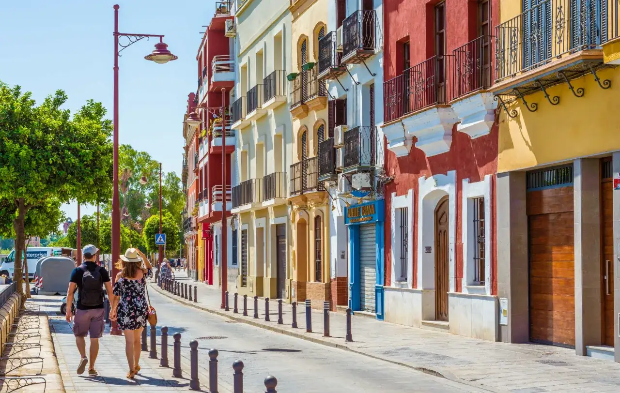 Ein Paar spaziert entlang bunter H&auml;user in Sevilla. Entdecken Sie hier die besten Sevilla Geheimtipps f&uuml;r Ihren Urlaub.