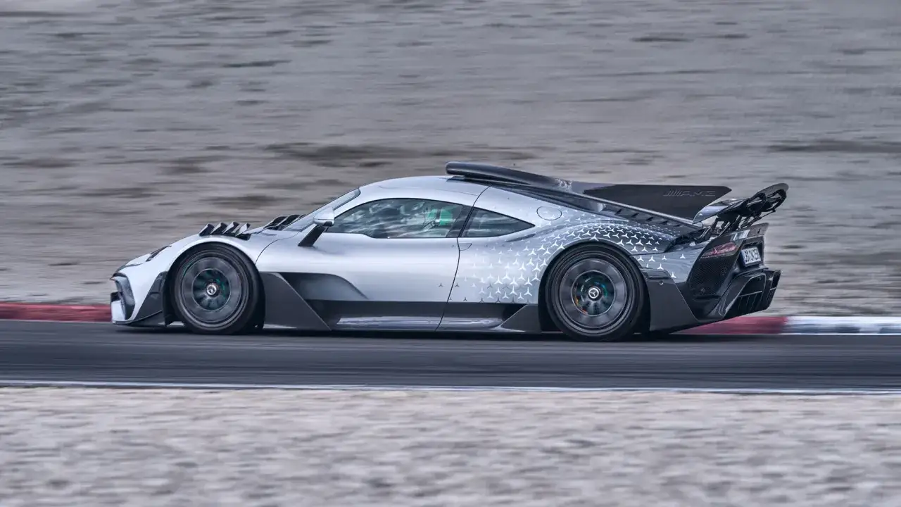 Srebrny Mercedes-AMG ONE pędzi po torze wyścigowym, jego aerodynamiczne linie i wzory na karoserii podkreślają jego wyścigowe dziedzictwo.