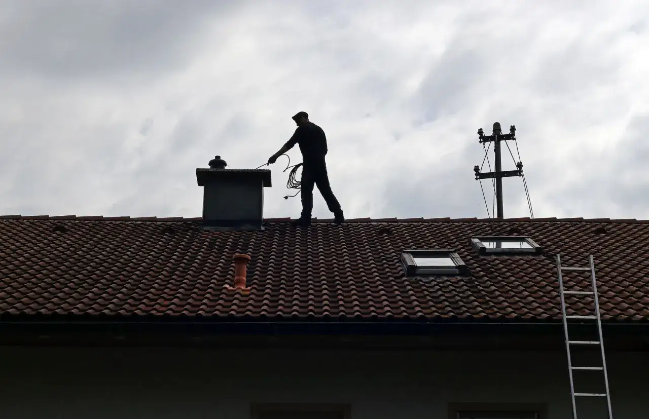 Ciekawe, ile kosztuje murowanie komina? Kominiarz na dachu sprawdza stan techniczny.