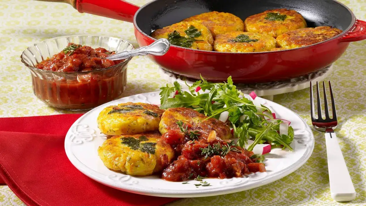 Goldbraune vegetarische Frikadellen mit frischem Salat und Tomaten-Chutney, serviert in einer roten Pfanne und auf einem Teller.