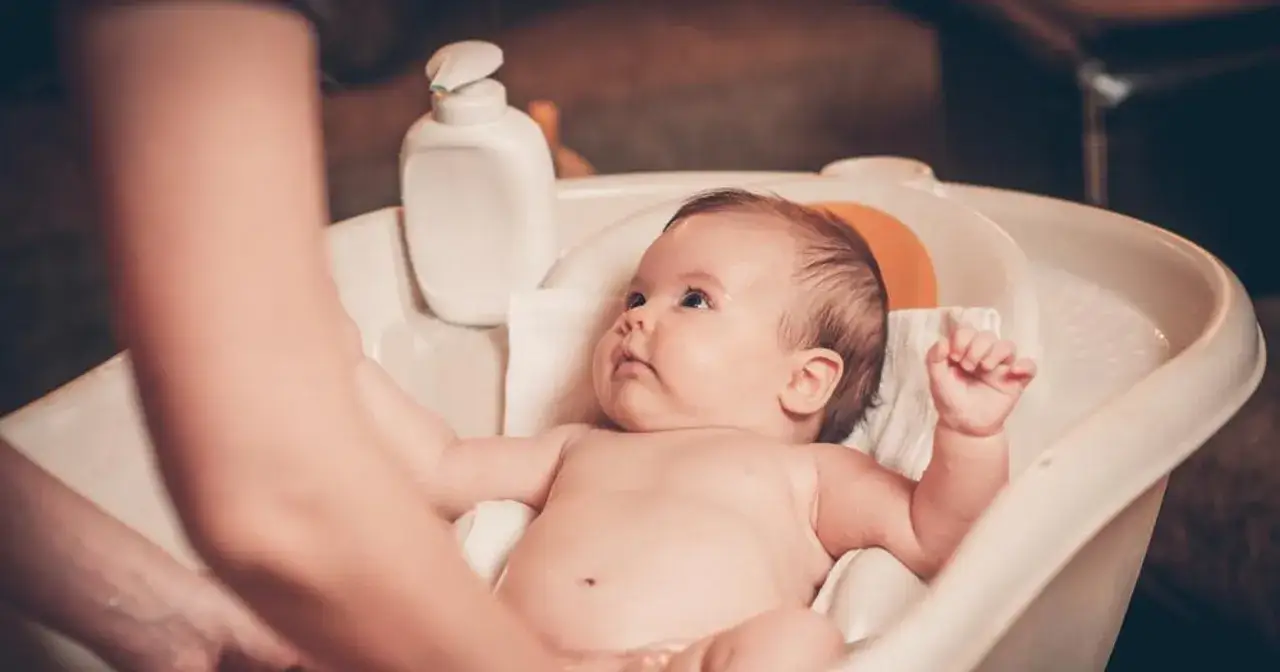 Malutkie dziecko pluska się w wanience dla niemowlaka. Obok stoi buteleczka z kosmetykiem.