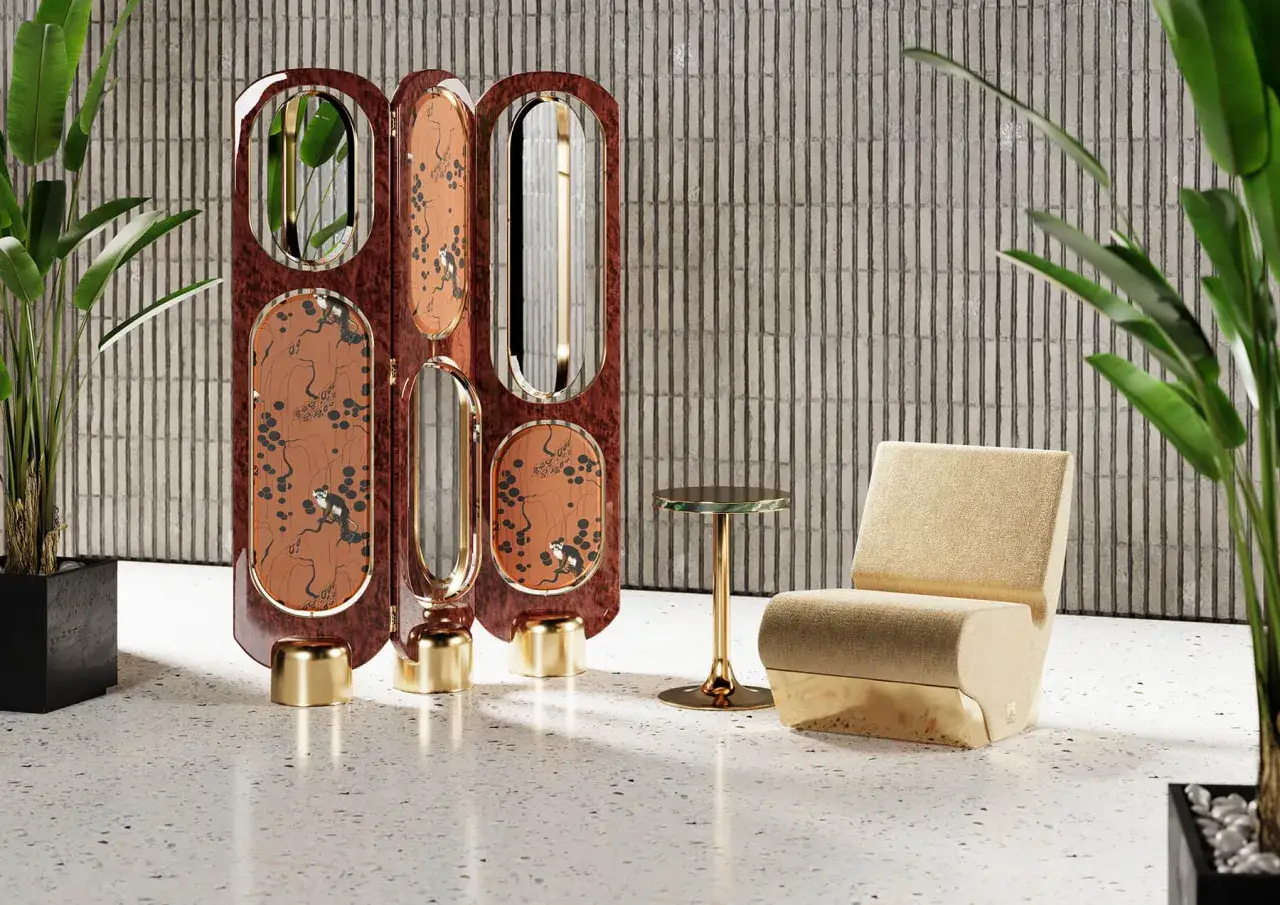Un paravento decorato con scimmie e rami, in un elegante stile jungle chic, accanto a una poltrona dorata e piante verdi.