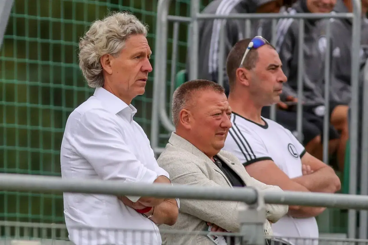 Marek Śledź w białej koszuli, obok mężczyźni w strojach sportowych, obserwują wydarzenia.