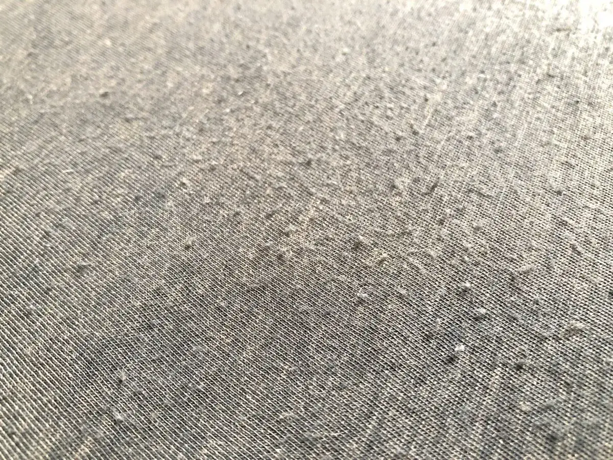 Nahaufnahme eines grauen Stoffes, auf dem kleine Kn&ouml;tchen sichtbar sind. Es zeigt, wie **merinowolle fusselt**, ein Zeichen f&uuml;r Abnutzung.