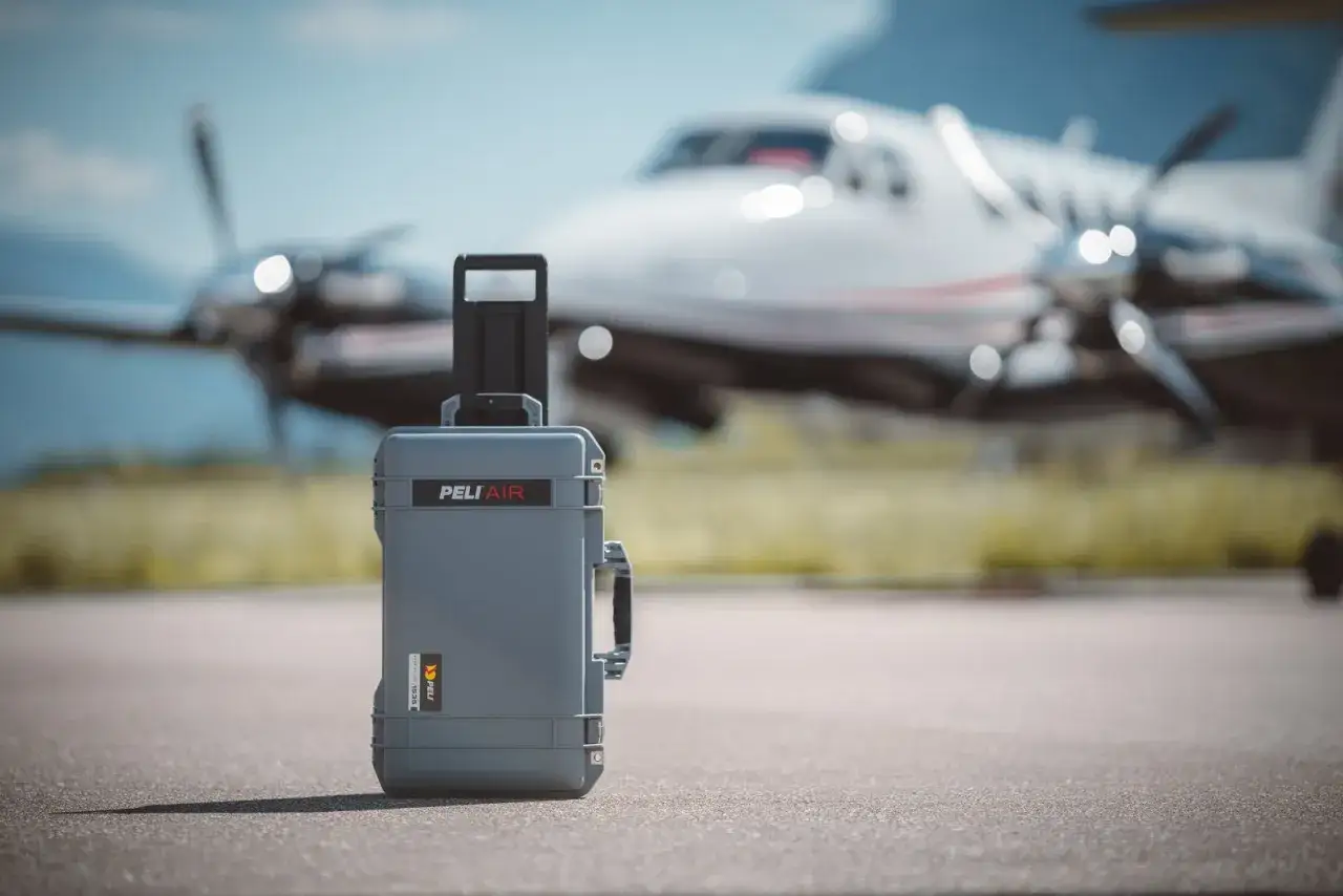 Gr&aring; Peli Air-v&auml;ska, perfekt handbagage p&aring; flyg, st&aring;r p&aring; asfalten framf&ouml;r ett litet privatplan.