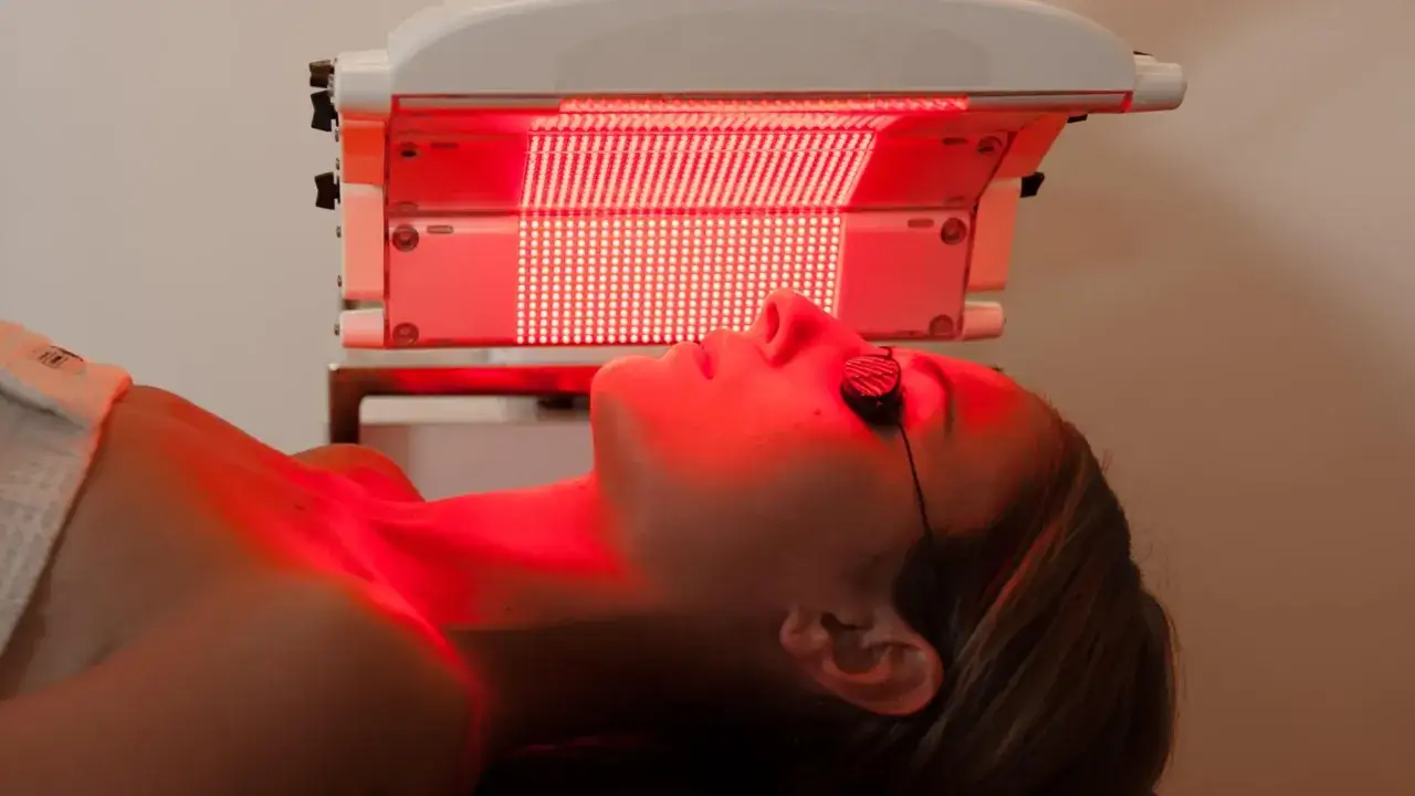 Donna con occhiali protettivi sotto una lampada per fotobiomodulazione. Informarsi sulle controindicazioni prima del trattamento.