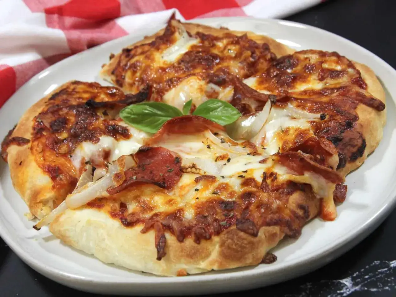 Pyszna pizza z piekarnika beztłuszczowego (air fryer) z serem, salami i cebulą, ozdobiona listkiem bazylii.