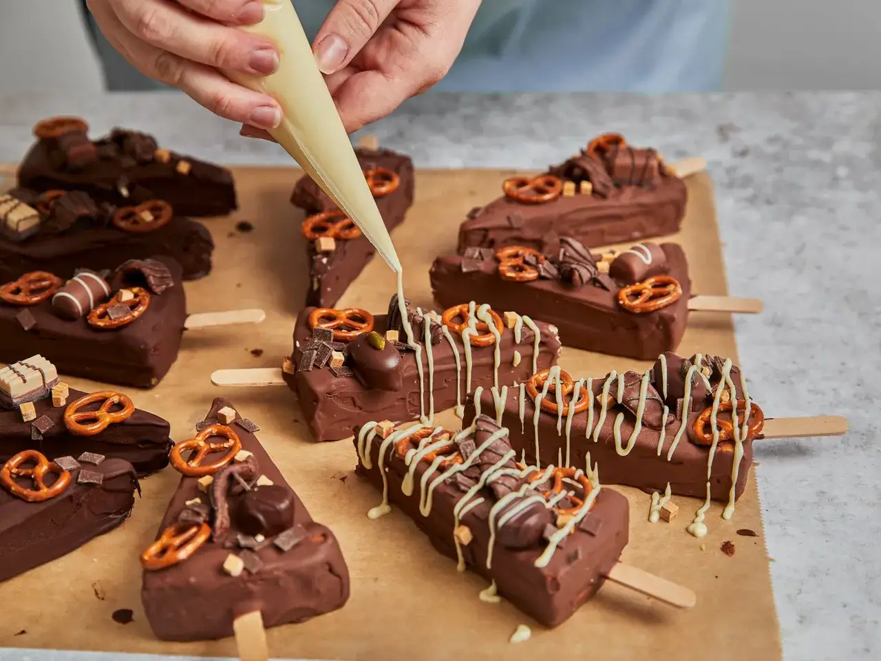 Schokoladige Cheesecake-Sticks mit Brezeln und Karamellstücken werden mit weißer Schokolade verziert.