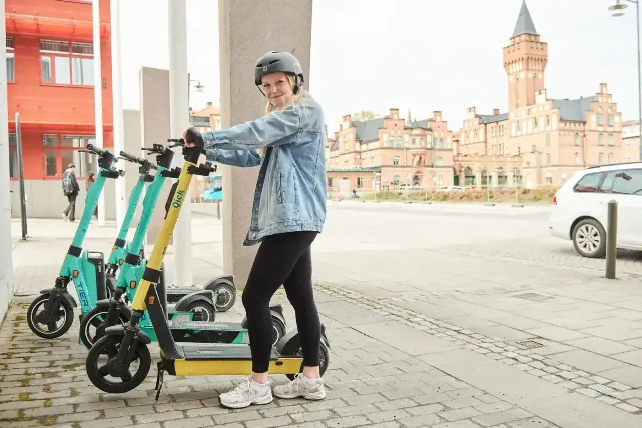 En tjej med hj&auml;lm st&aring;r vid flera elsparkcyklar. Hon funderar p&aring; om man f&aring;r &aring;ka tv&aring; p&aring; elsparkcykel, men reglerna s&auml;ger nej.