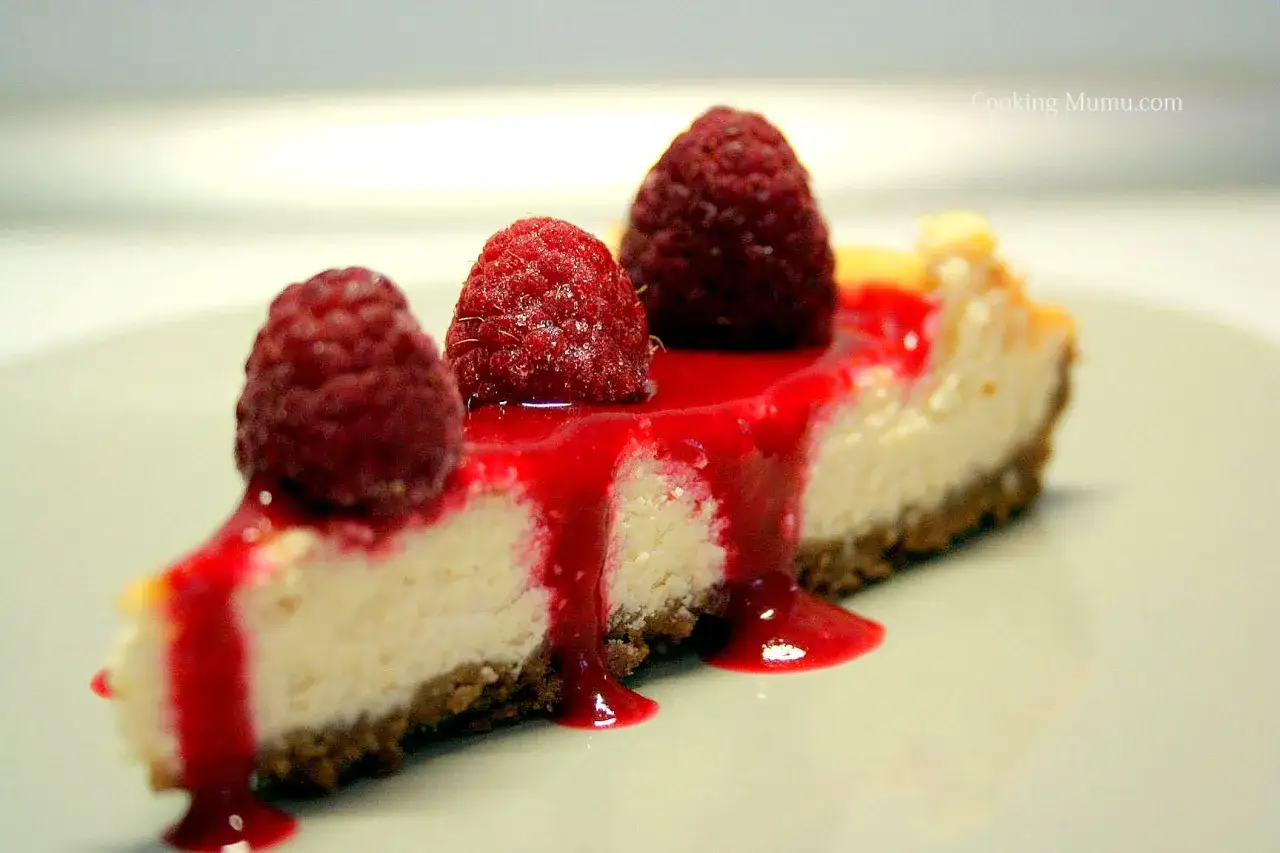 Tranche de cheesecake garnie de framboises fra&icirc;ches et napp&eacute;e d'un coulis de framboise onctueux.