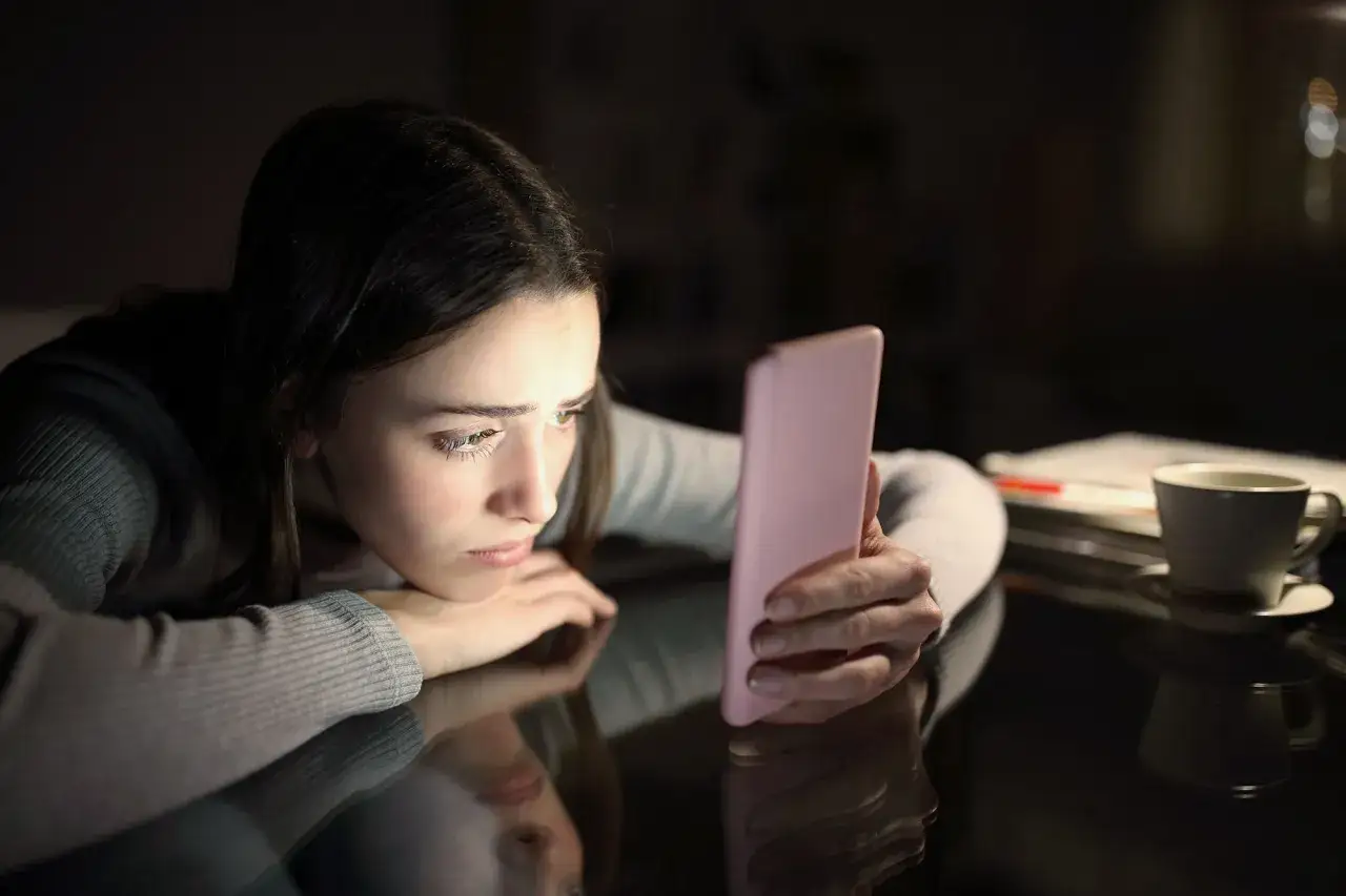 Zmartwiona dziewczyna patrzy na telefon, czując FOMO. Co to za uczucie?