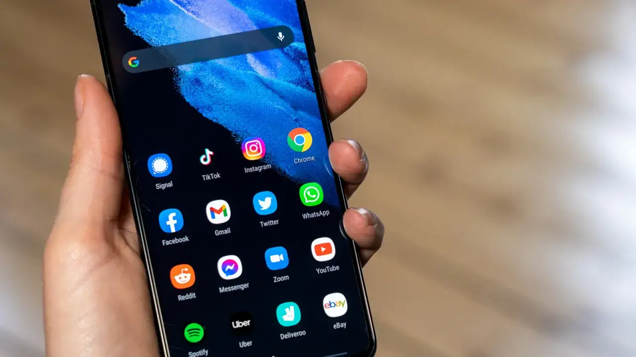 Dłoń trzyma smartfon z ikonami aplikacji. Chcesz wiedzieć, jak zmniejszyć czułość ekranu dotykowego? Sprawdź ustawienia telefonu.