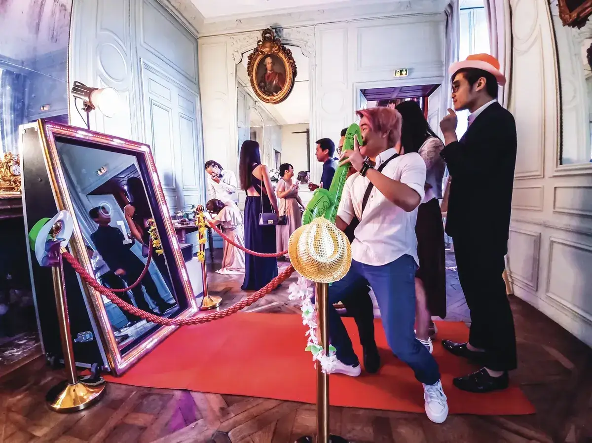 Des invit&eacute;s s'amusent devant un photobooth interactif, avec des ballons gonflables et des chapeaux pour des souvenirs m&eacute;morables.