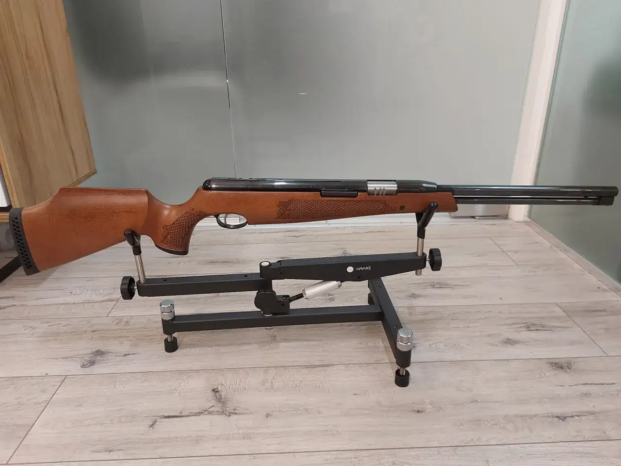 Elegancki karabin pneumatyczny Air Arms TX200 z drewnianą osadą, prezentowany na czarnym stojaku Hawke.