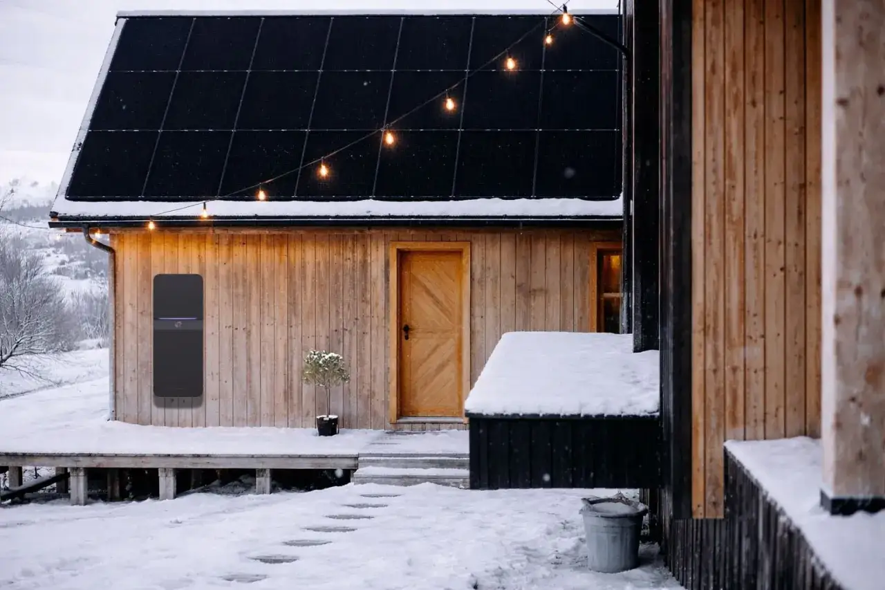 Vintervackert hus med solceller p&aring; taket och en batterilagringsenhet p&aring; v&auml;ggen. Perfekt f&ouml;r att spara kwh till vintern.