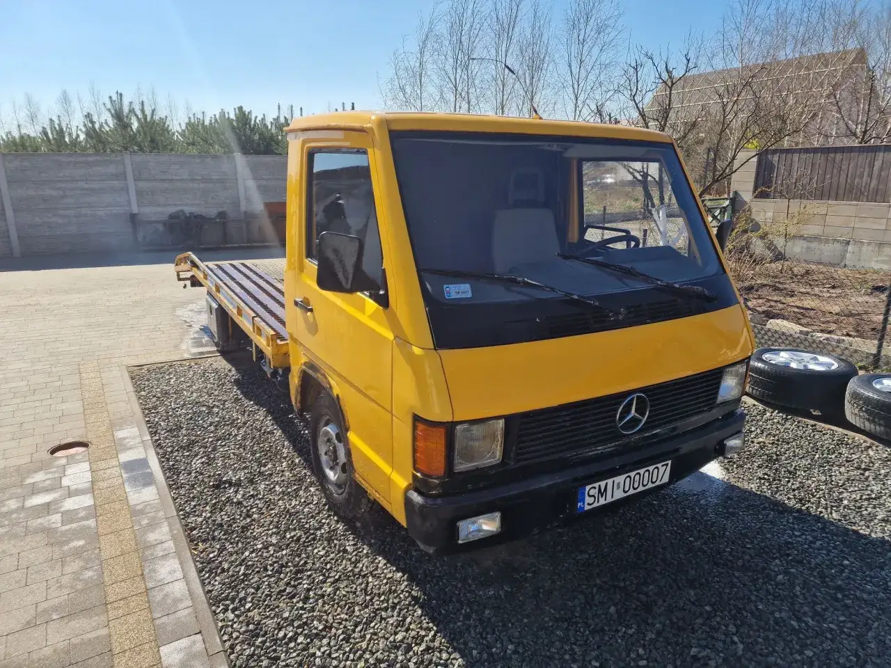 Żółty Mercedes MB 100 z platformą do transportu, gotowy do akcji.