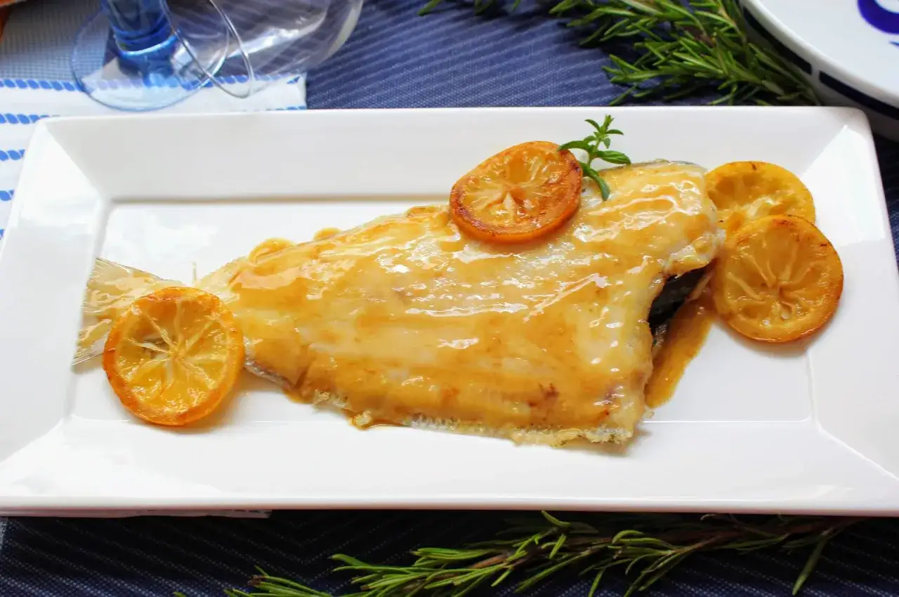 Delicioso gallo a la plancha ba&ntilde;ado en salsa dorada, decorado con rodajas de lim&oacute;n caramelizado y ramitas de romero fresco.