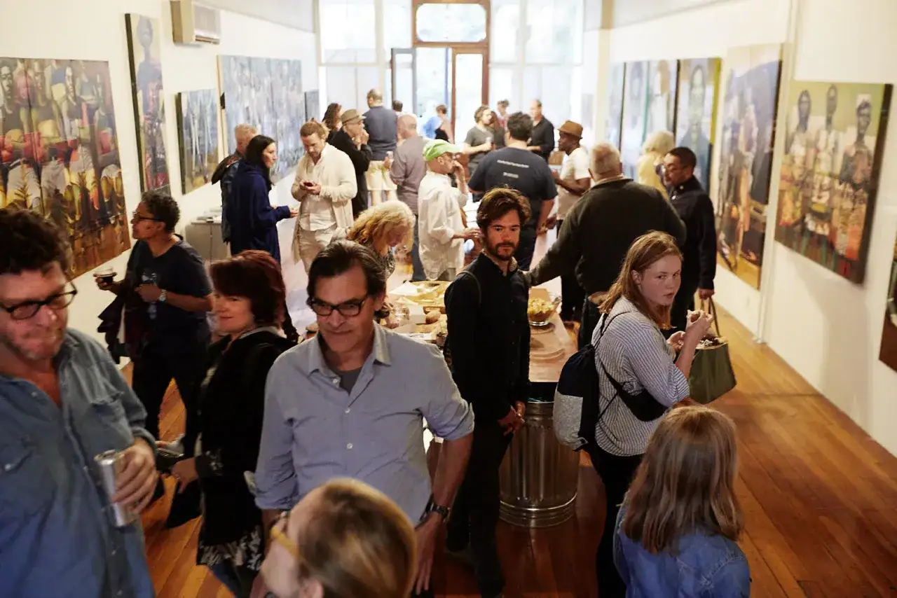 People mingle at the robin rice gallery, admiring artwork on the walls.