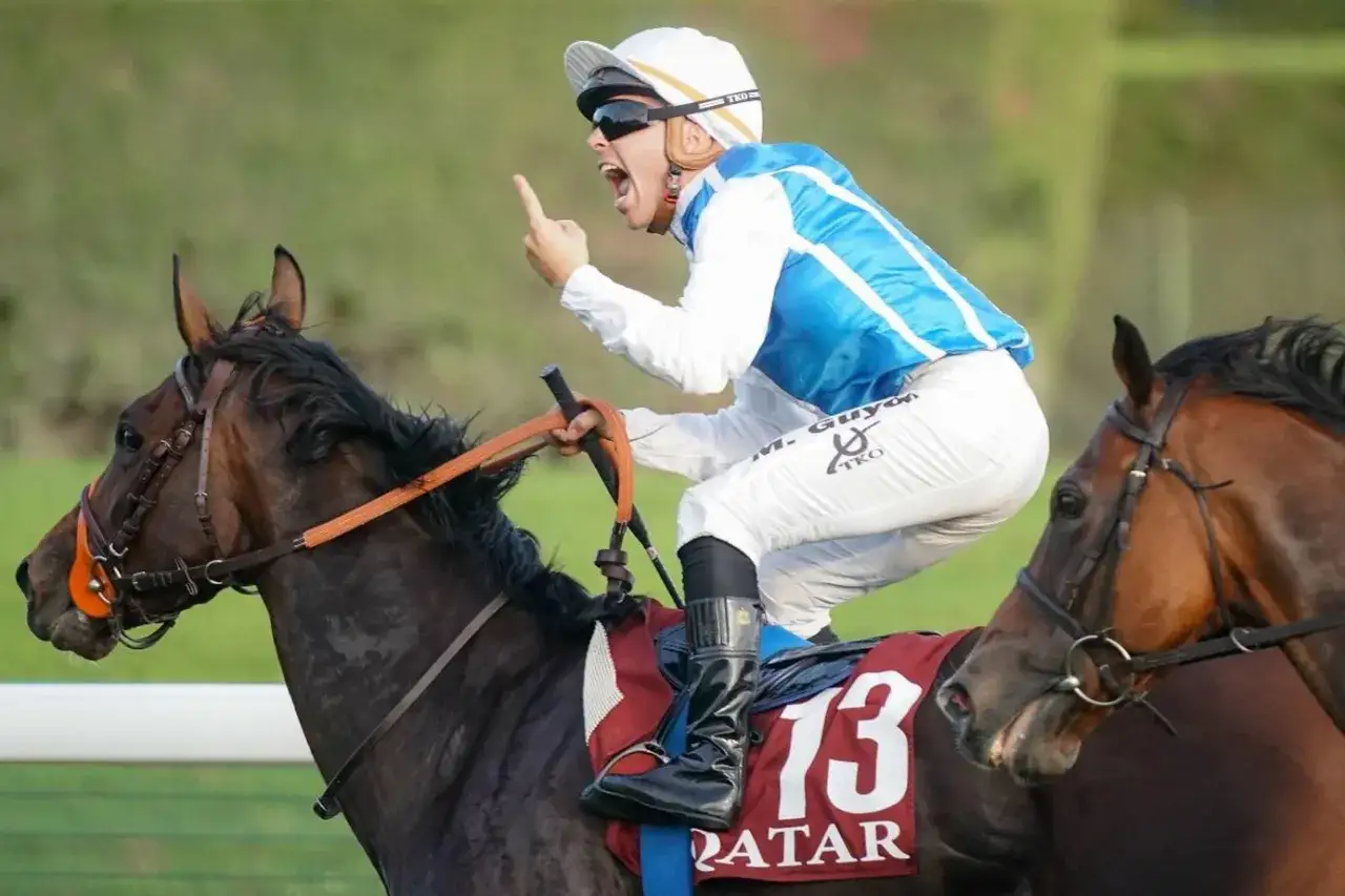 Un jockey exulte sur son cheval, le doigt lev&eacute;, c&eacute;l&eacute;brant une victoire.